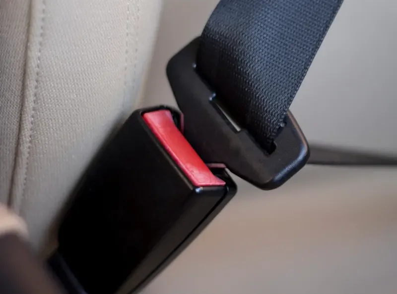 Black seat belt buckle receiver with a red release button mounted beside a vehicle seat