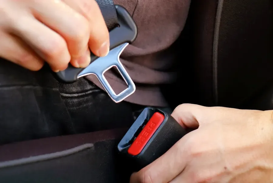Hands inserting a seat belt latch plate into the buckle receiver during a fitment check