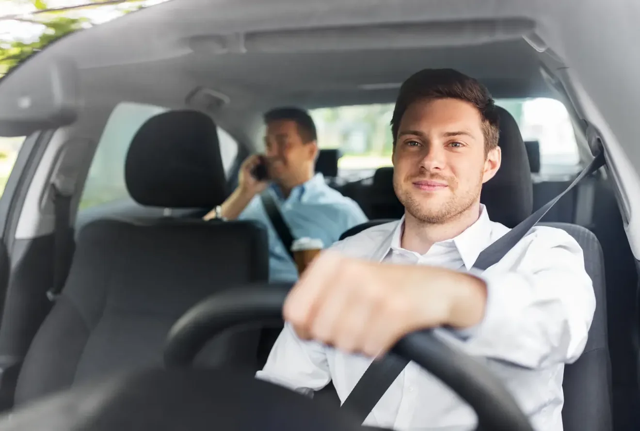Driver seated at the wheel of a car wearing a fastened three-point seat belt, with a passenger behind