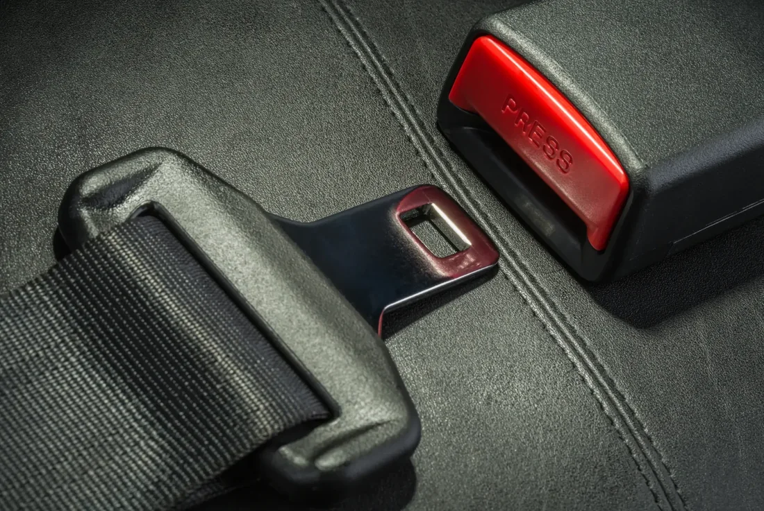 Three-point seat belt latch plate engaged in its buckle receiver, showing the red release button